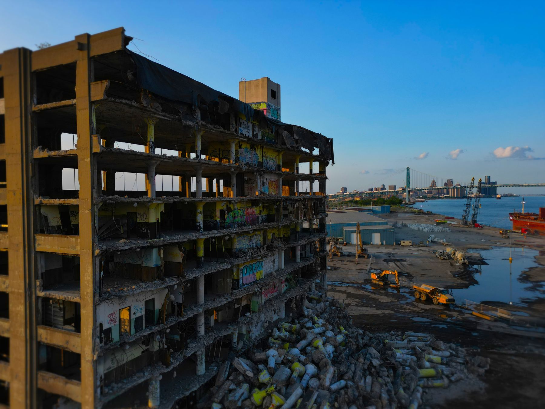 Aerial view of a gutted building on the Detroit riverfront at sunset, with the Ambassador Bridge behind