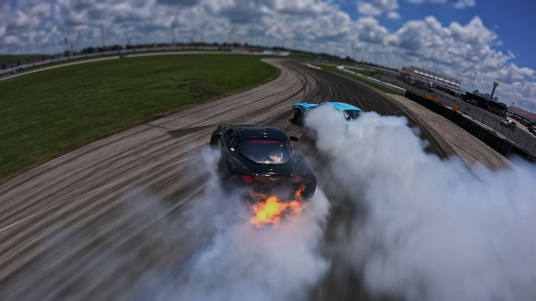 Two drift cars sliding in tandem with flames from the exhaust, filmed from an FPV drone